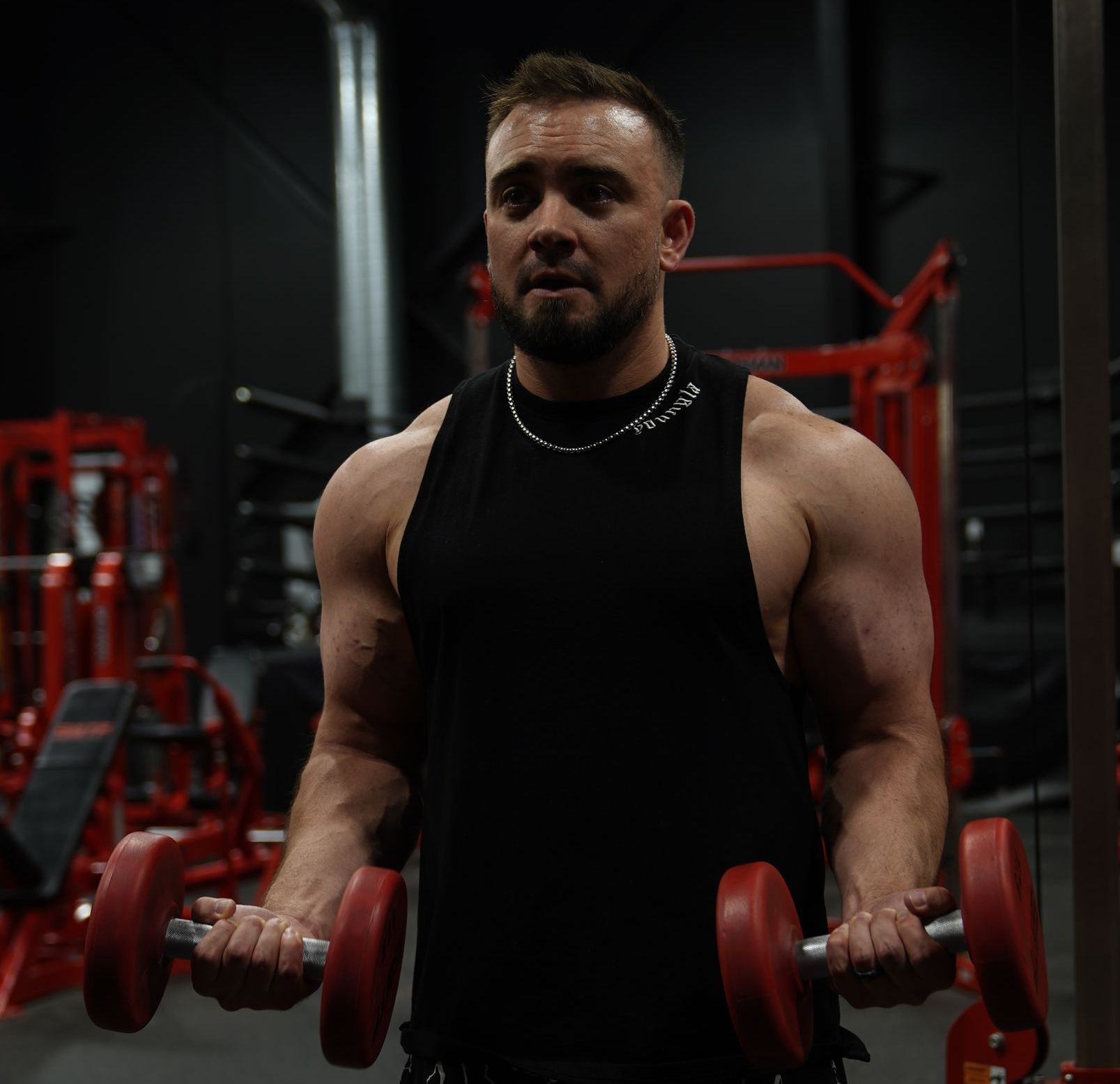 A man in a black tank top is lifting dumbbells in a gym.