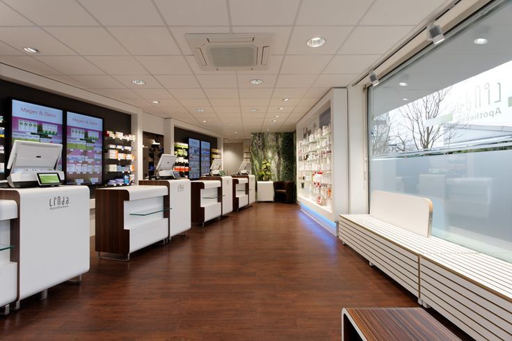 Innenansicht einer gut beleuchteten Apotheke mit dunklen Holzböden, weißen Theken und Produktauslagen.
