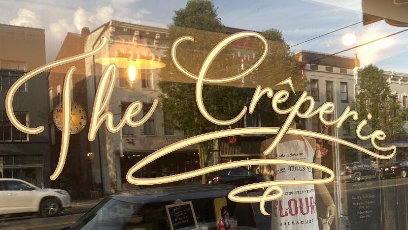 A sign for the creperie is written on a window.