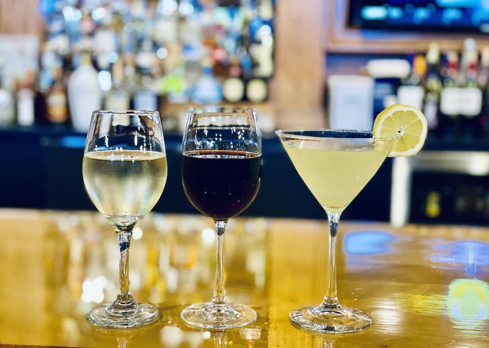 Two glasses of wine and a martini are sitting on a bar.
