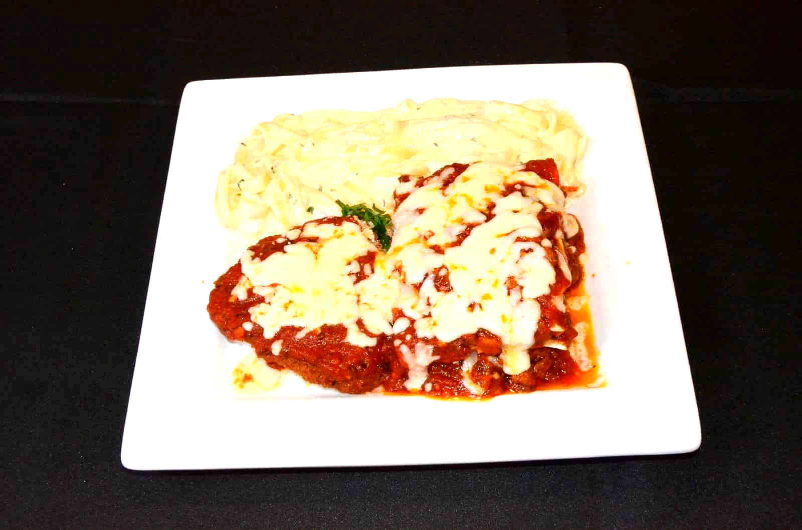 Chicken Parmesan with spaghetti on a white square plate.