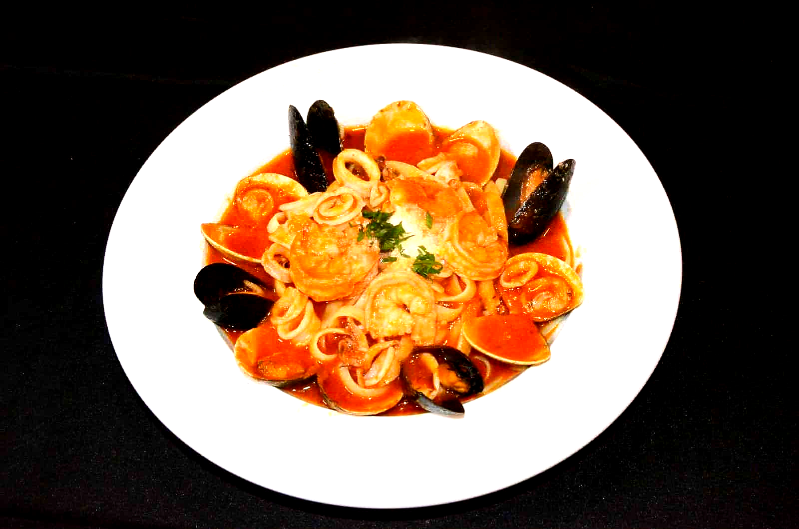 Seafood pasta dish on a white plate; includes shrimp, mussels, and squid rings in red sauce.