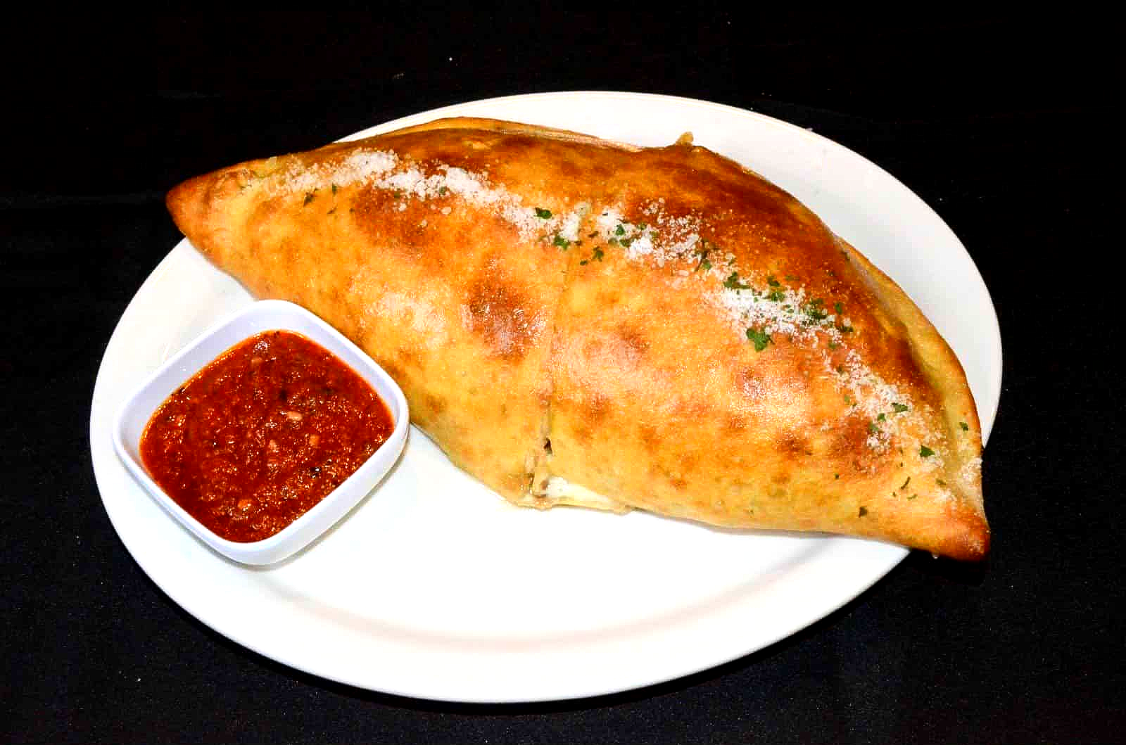 Calzone on white plate with a side of red sauce.