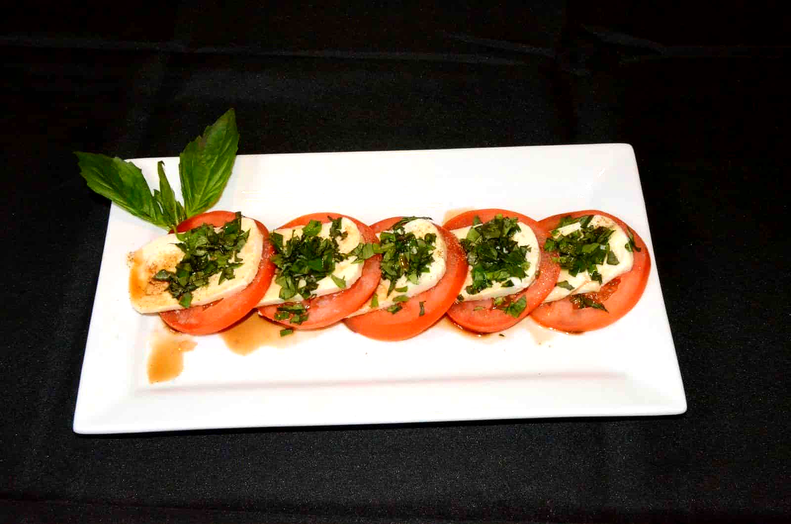 Tomato and mozzarella salad with basil and balsamic glaze on a white plate.