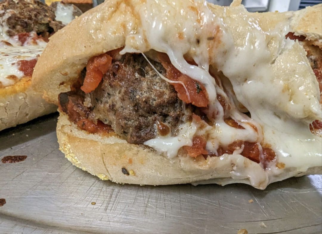 A close up of a meatball sandwich with cheese on a plate.