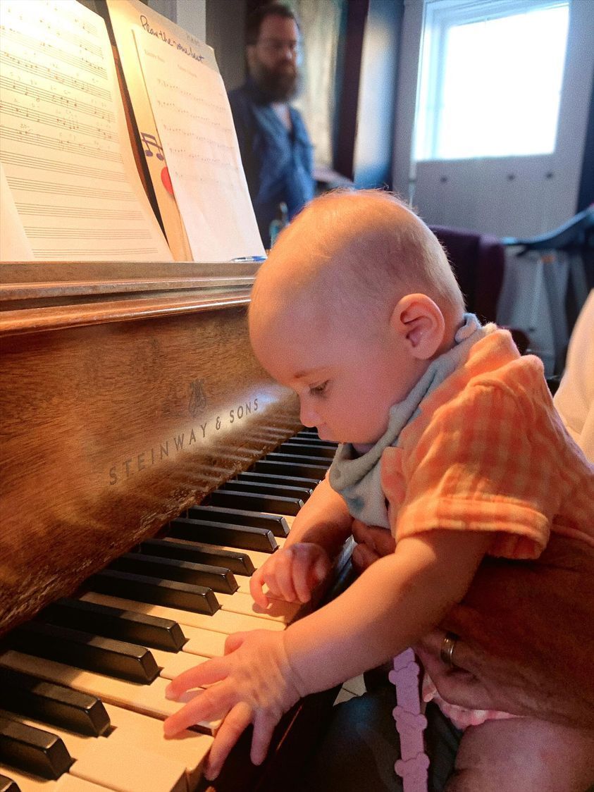 A baby is playing a piano with a man in the background