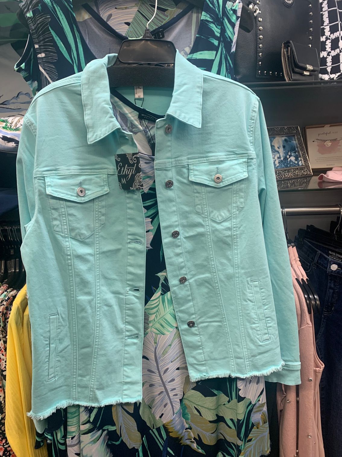A light blue denim jacket is hanging on a hanger in a store.