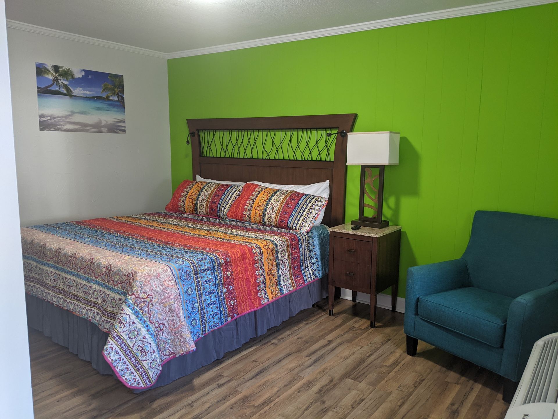 A hotel room with a bed , chair , nightstand , lamp and green wall.