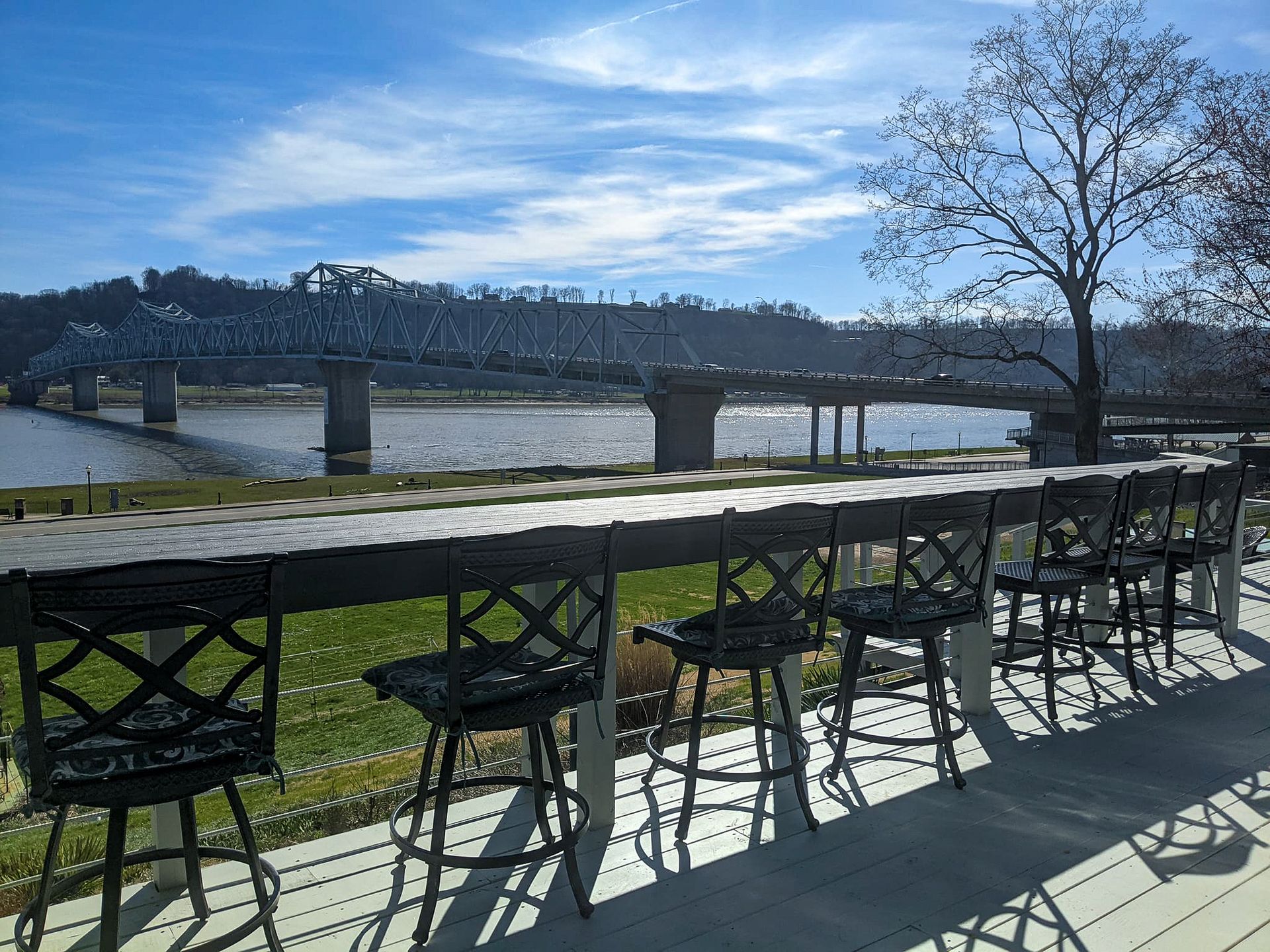 A row of chairs on a deck overlooking a river with a bridge in the background