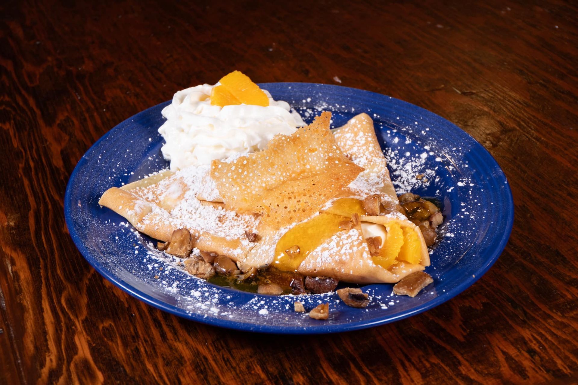 A blue plate topped with a crepe and whipped cream
