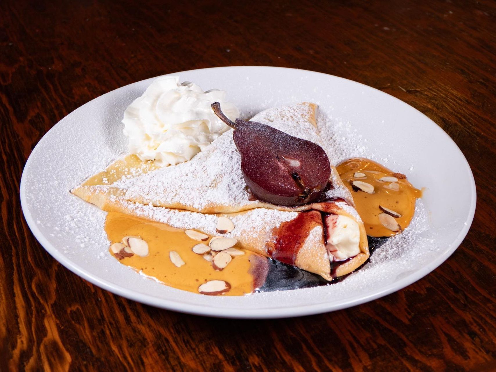 A white plate topped with a dessert crepe with whipped cream and powdered sugar