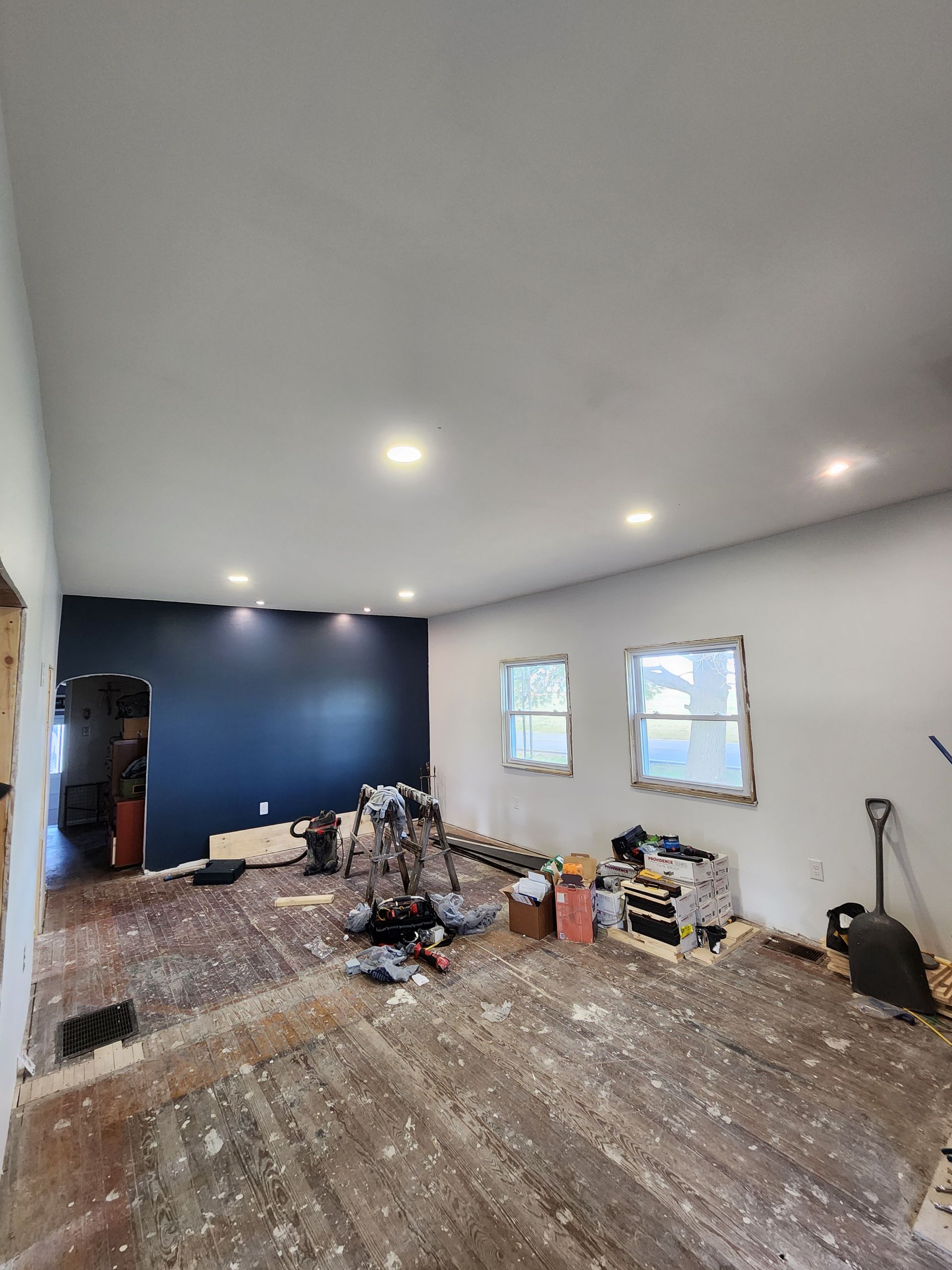 A large room with a wooden floor and a blue wall is being remodeled.