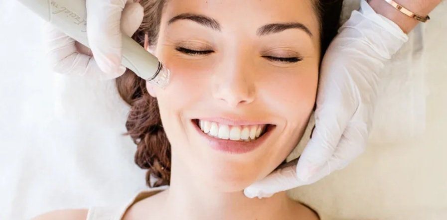 A woman is smiling while getting a facial treatment.