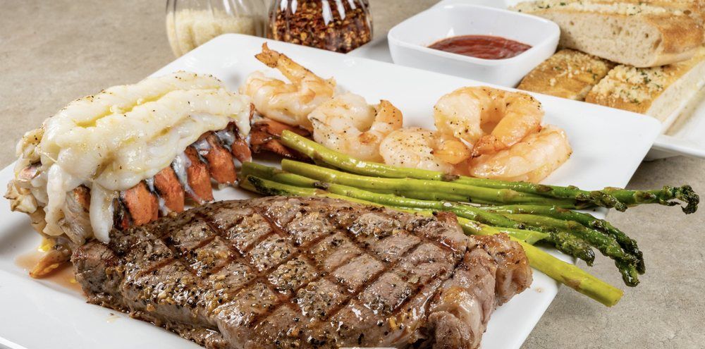A white plate topped with a steak , shrimp and asparagus.
