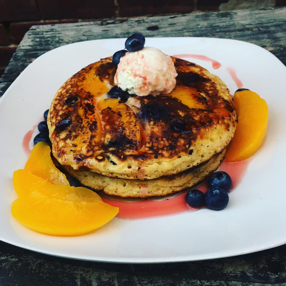 A stack of pancakes with blueberries and peaches on a white plate