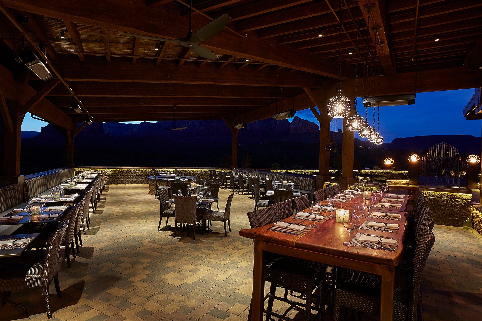 Outdoor dining patio at dusk, tables set with chairs, string lights, mountains in the background. Mariposa Sedona