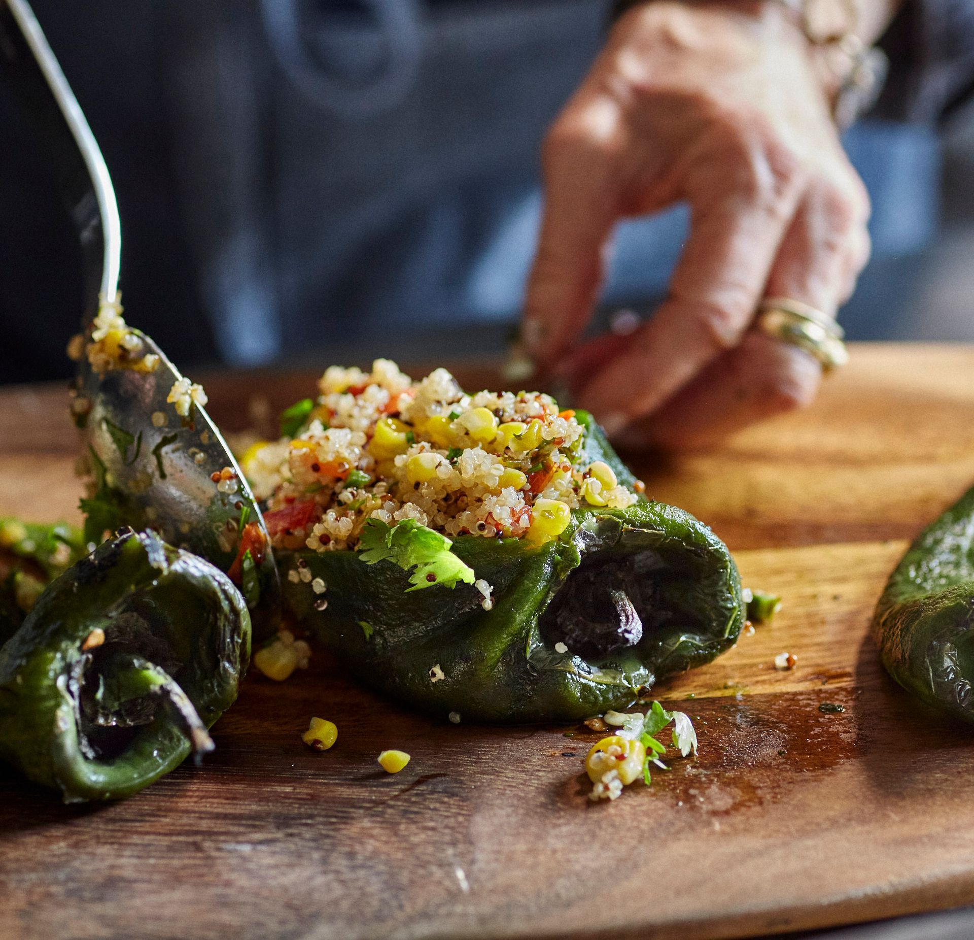 Stuffed poblano peppers on a wooden board being prepared with a spoon; hand reaching. Mariposa Sedona