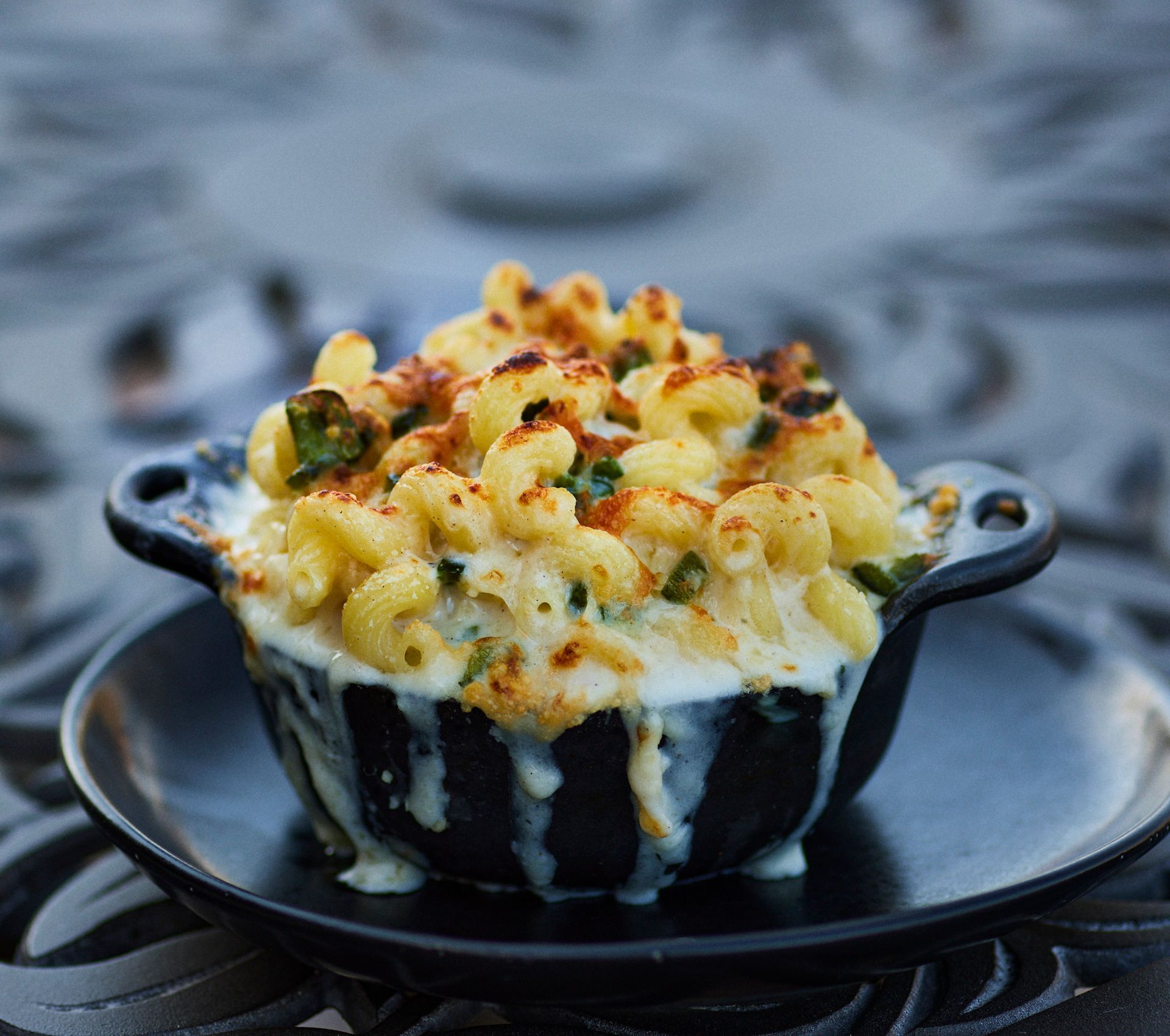 Mac and cheese in a black bowl on a plate, close up. Cheese is melted and bubbly. Mariposa Sedona