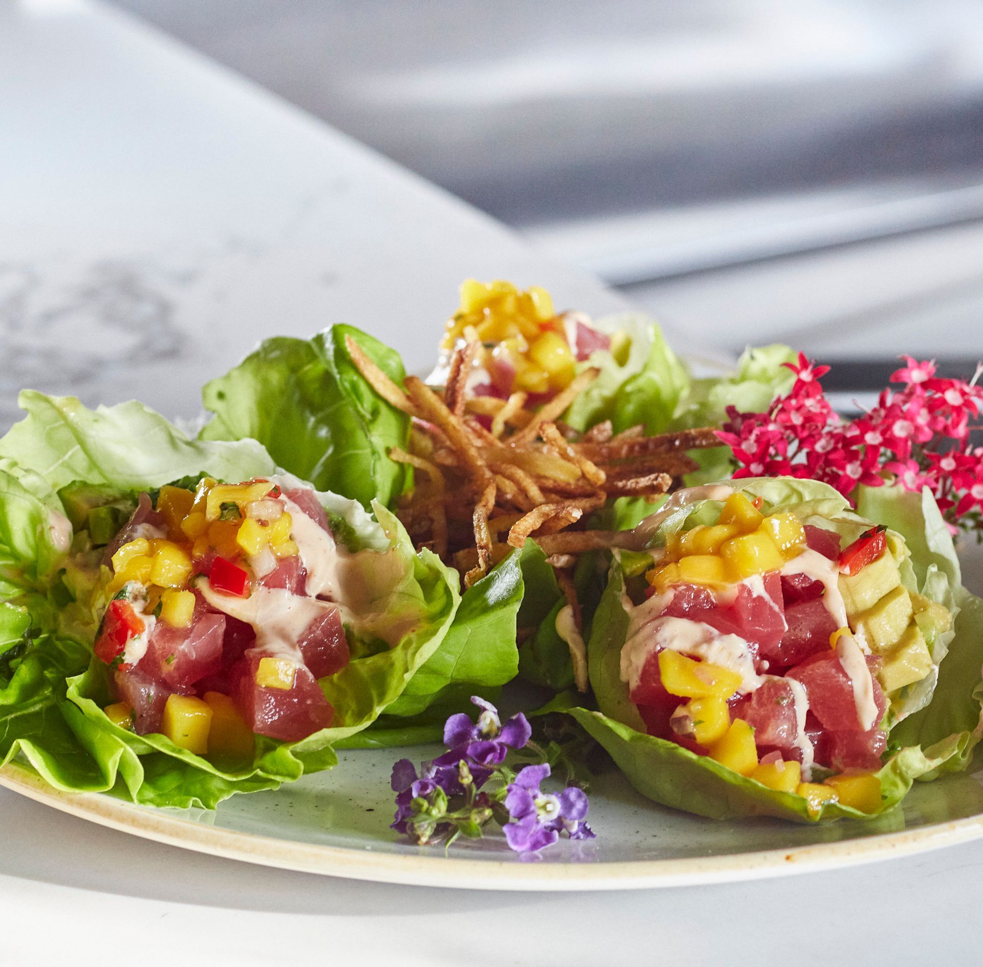 Lettuce wraps filled with tuna, mango salsa, and fried onions, garnished with flowers. Mariposa Sedona