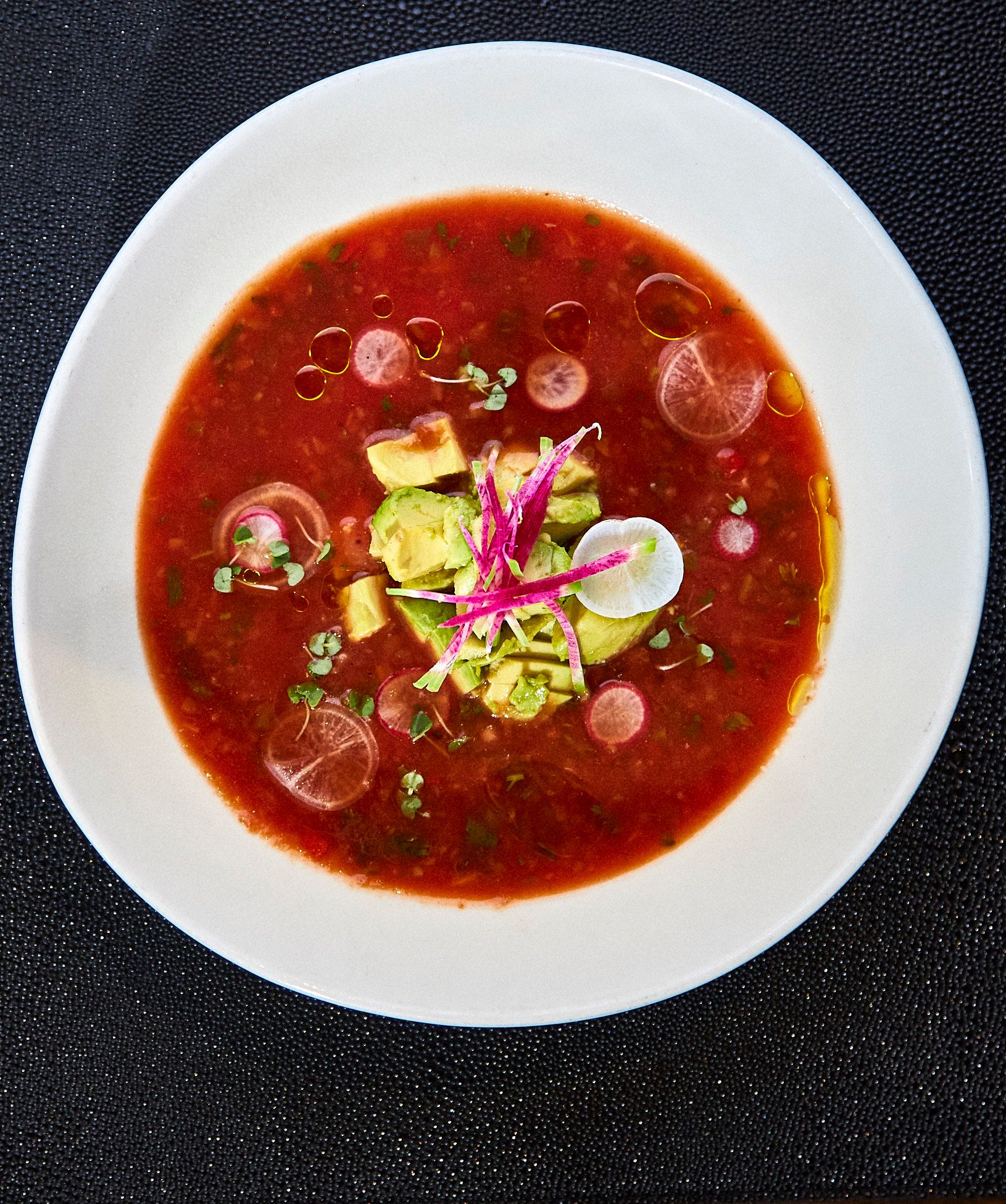 Gazpacho soup in white bowl; garnished with avocado, radish, and oil droplets. Mariposa Sedona