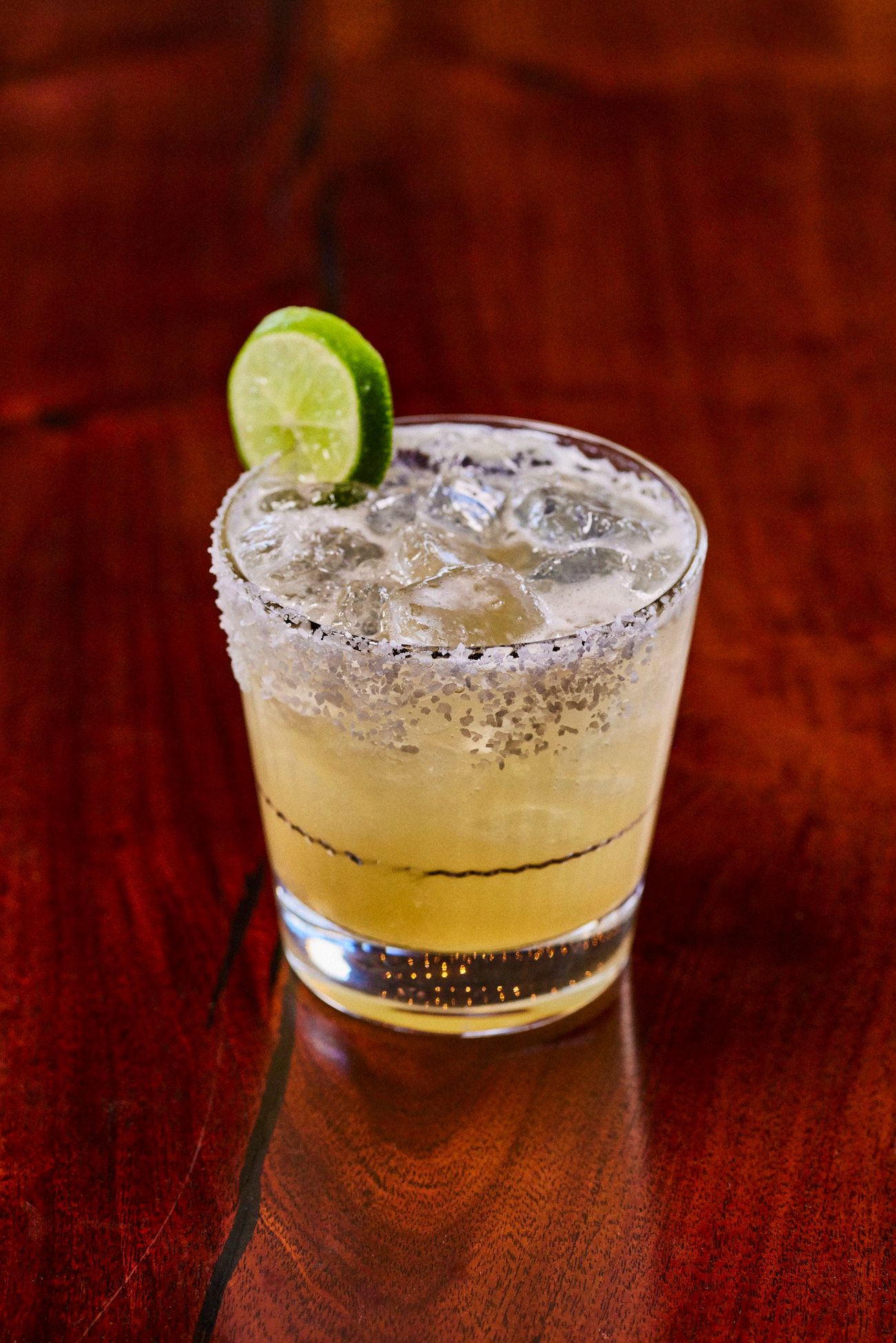 Margarita cocktail in a salt-rimmed glass, with a lime wedge, on a wooden table. Mariposa Sedona