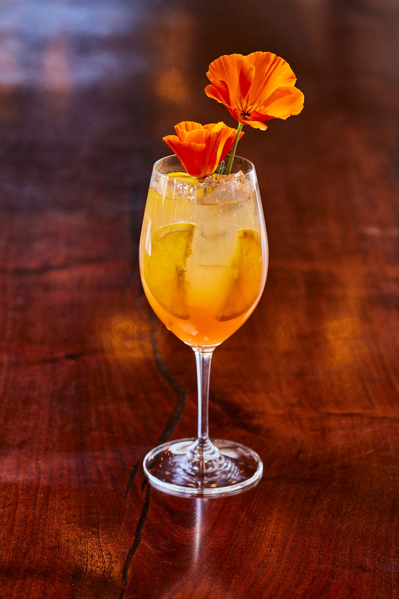 Cocktail in a stemmed glass, garnished with orange flowers, on a dark wood table. Mariposa Sedona