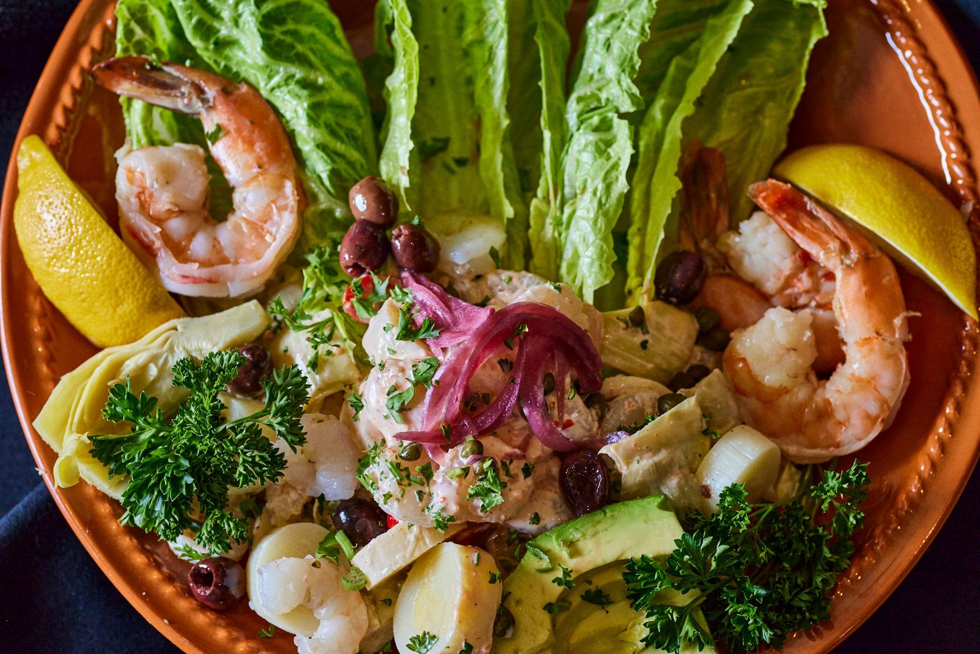 Shrimp and avocado salad with olives, lettuce, and lemon wedges on a brown plate. Mariposa Sedona