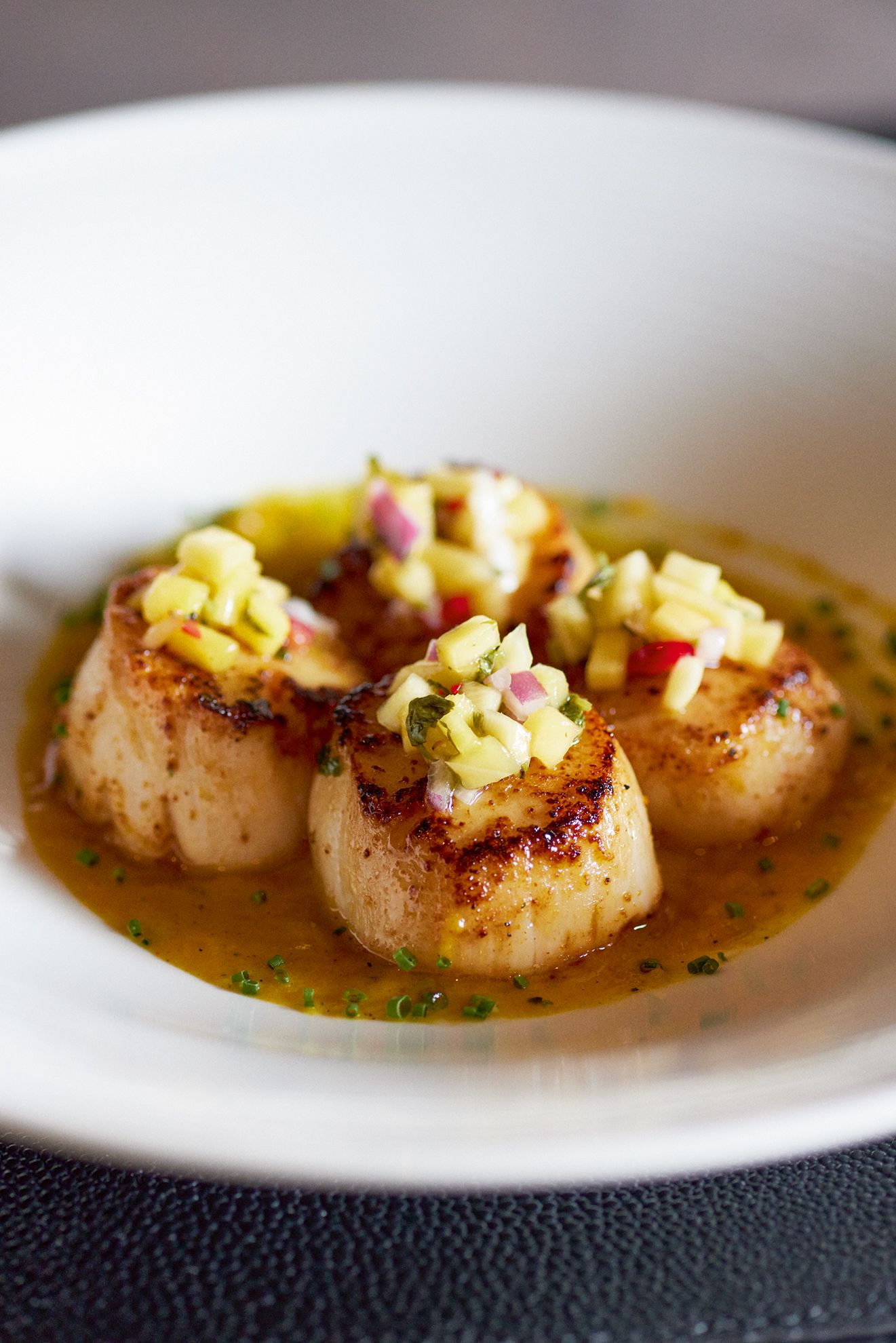 Seared scallops in sauce, topped with diced vegetables, in a white bowl. Mariposa Sedona