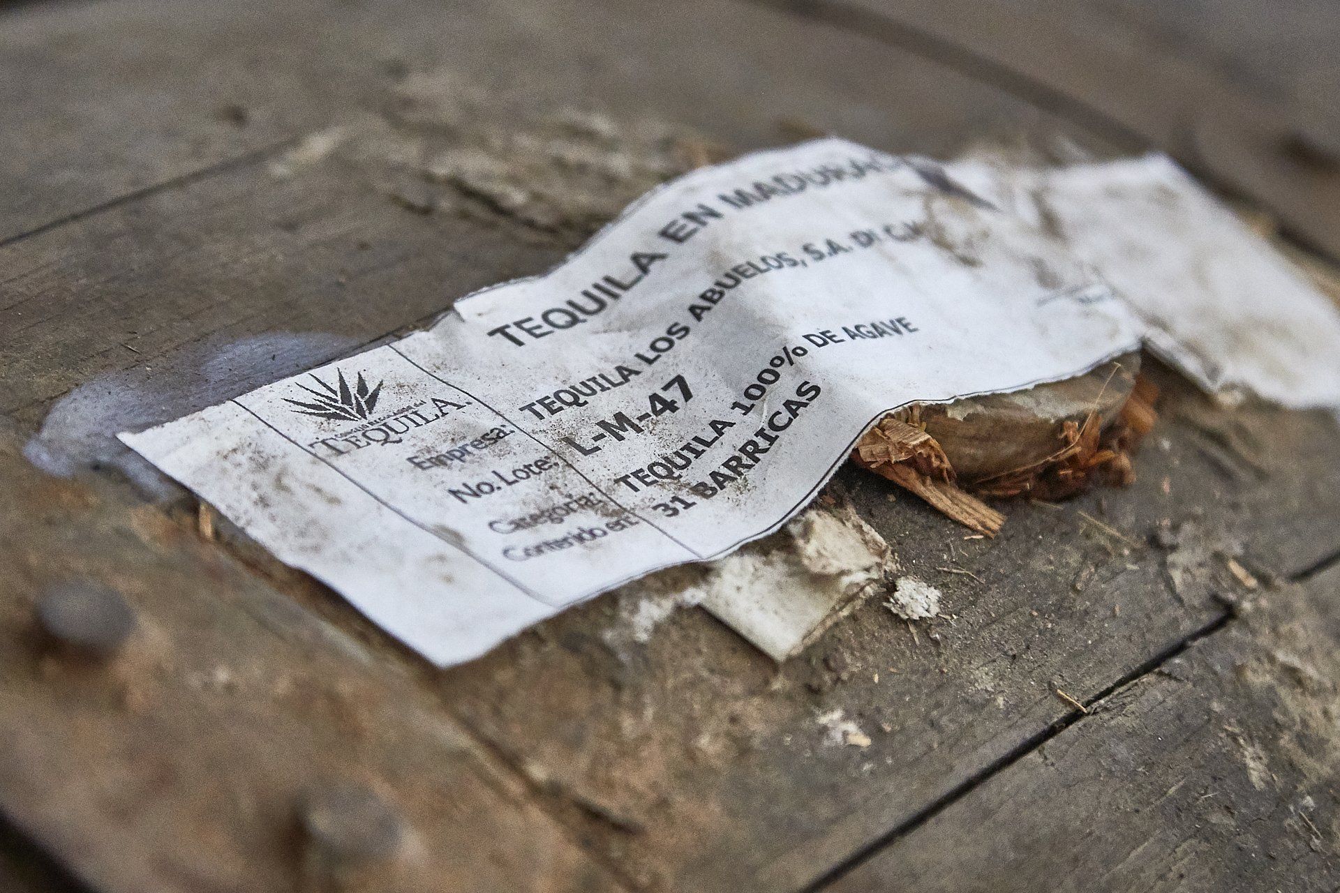 Close-up of a weathered wooden barrel with a partially torn label: