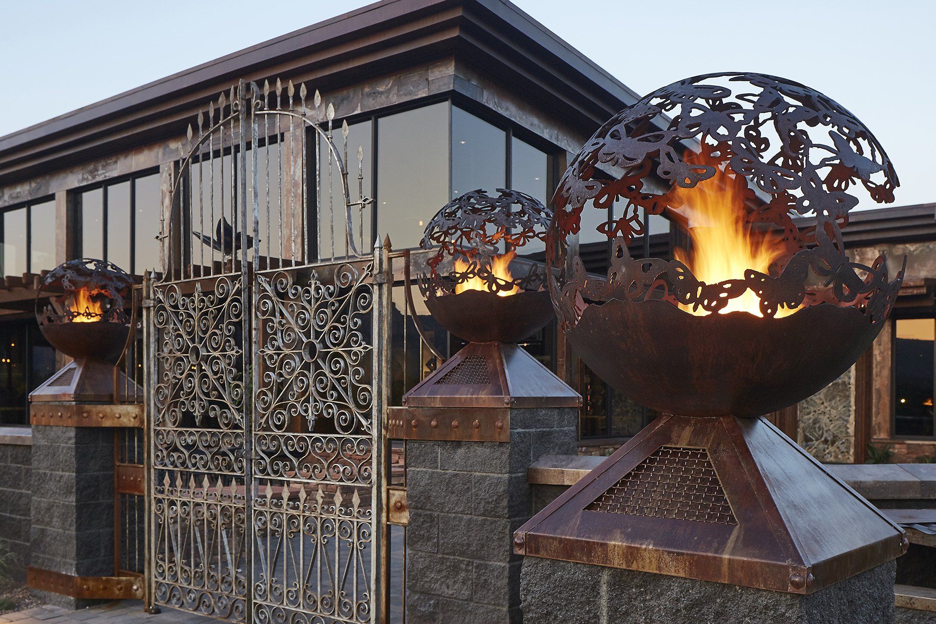 Three metal fire pits, one with a gate, outside a modern building; flames visible. Mariposa Sedona