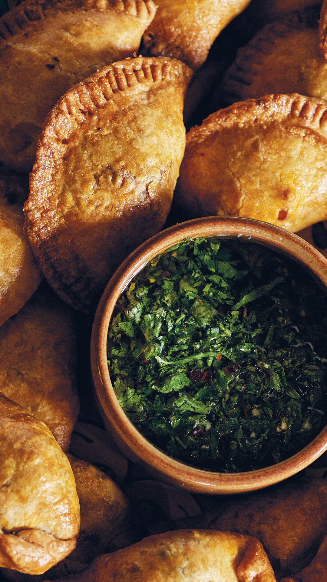 Golden-brown empanadas with a small bowl of green chimichurri sauce. Mariposa Sedona