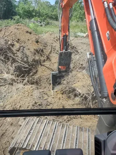 Inside excavator cab, digging in dirt with orange machinery; bright sky in background.