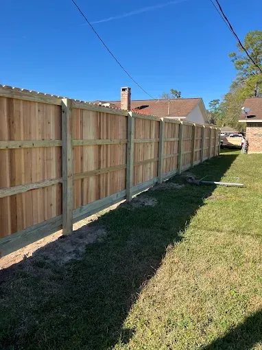 A new wooden fence stretches along a grassy yard under a clear blue sky.