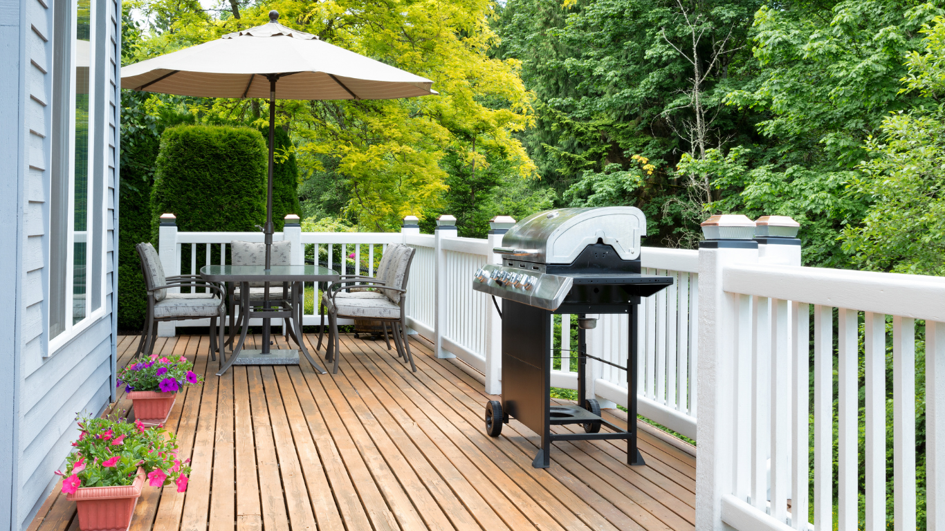 There is a grill on the deck with a table and chairs.