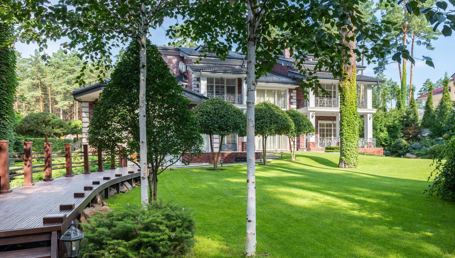 A large house is surrounded by trees and a lush green lawn.