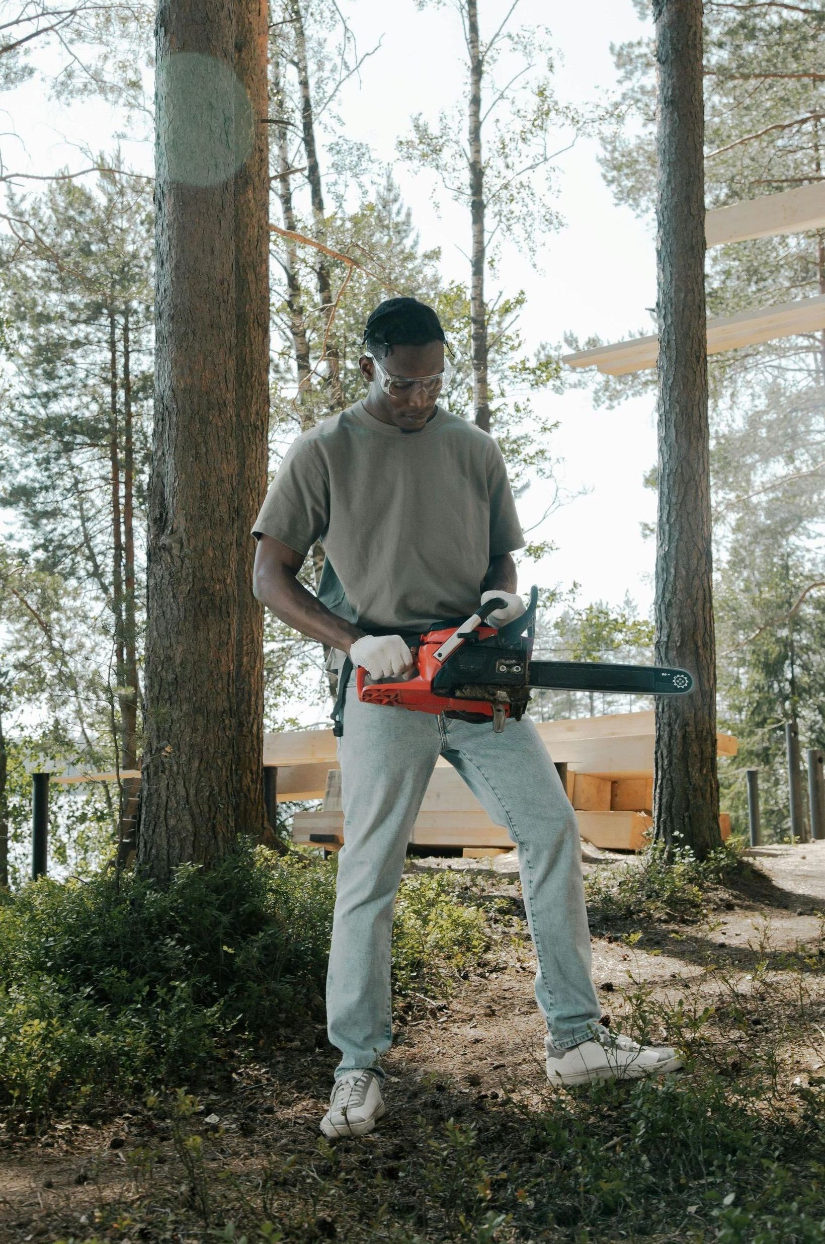 A man is standing in the woods holding a chainsaw.