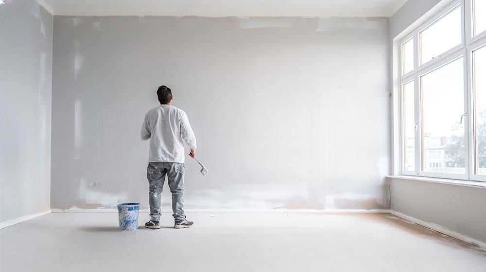 A man is painting a wall in an empty room.