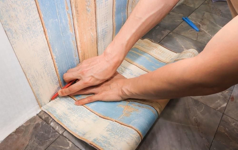 A person is measuring a piece of wallpaper with a pencil.