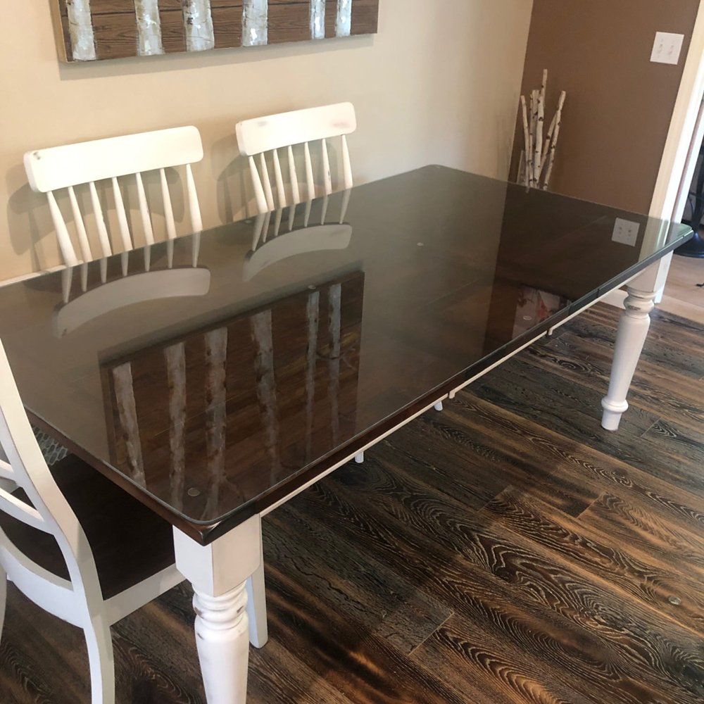 A dining room table with a glass top and white chairs.