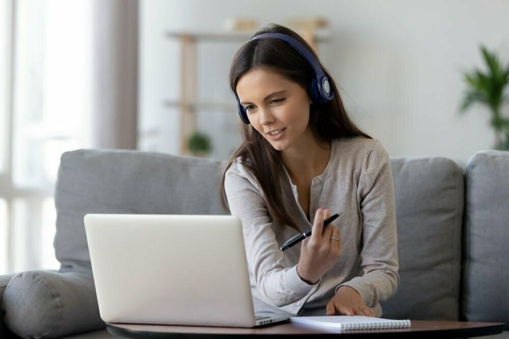 Une femme portant des écouteurs est assise sur un canapé en utilisant un ordinateur portable.