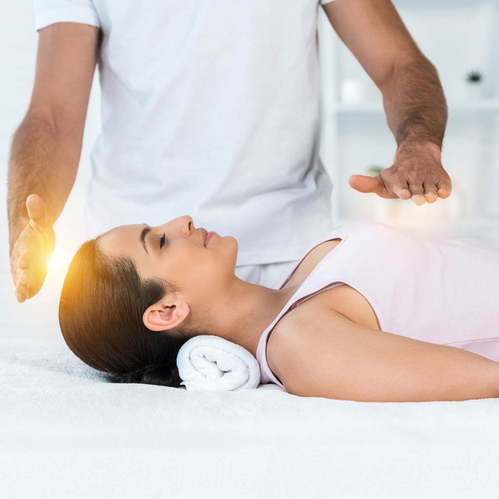 Une femme est allongée sur un lit et reçoit une séance de guérison de la part d'un homme.