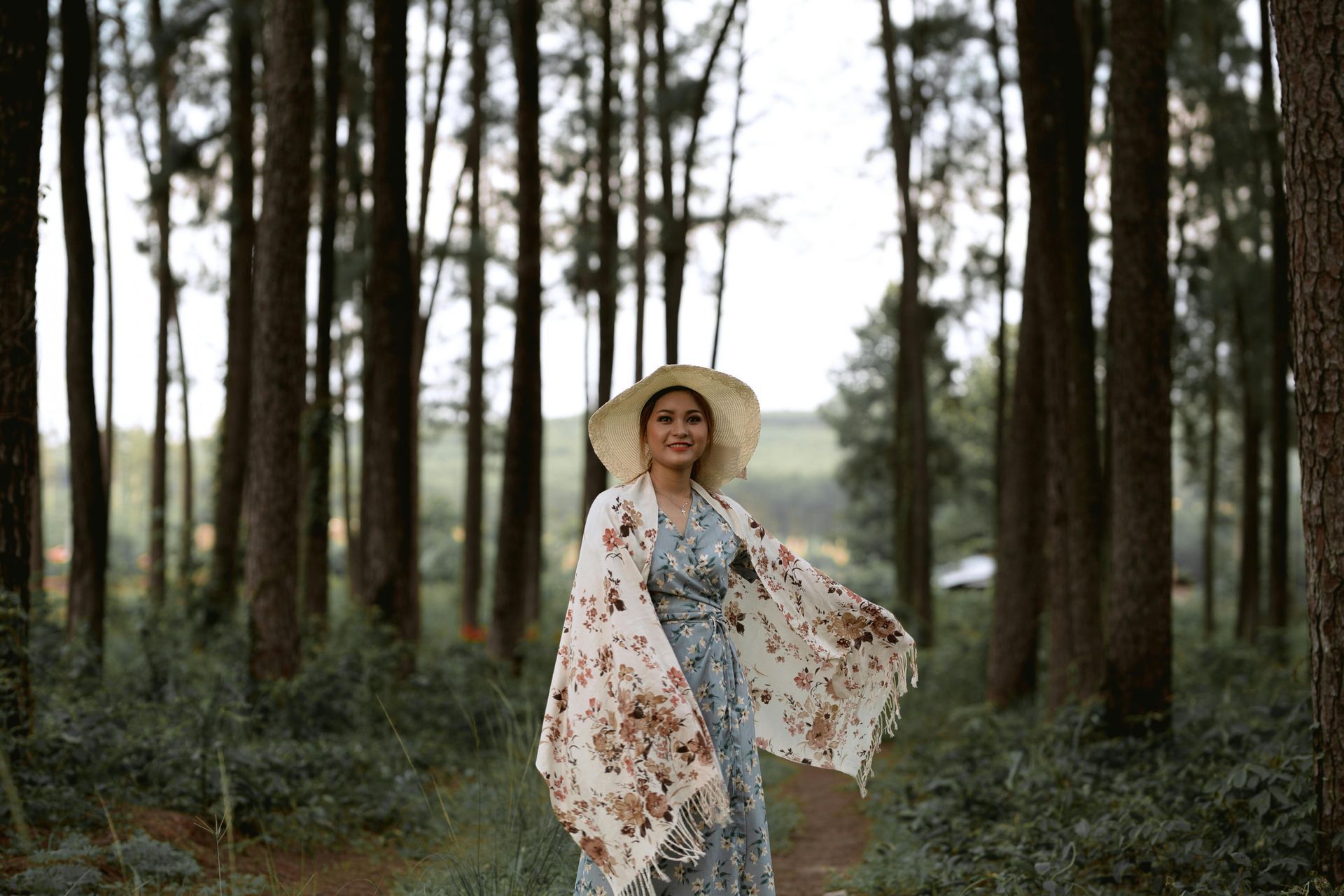 Une femme en robe et chapeau se tient au milieu d'une forêt.