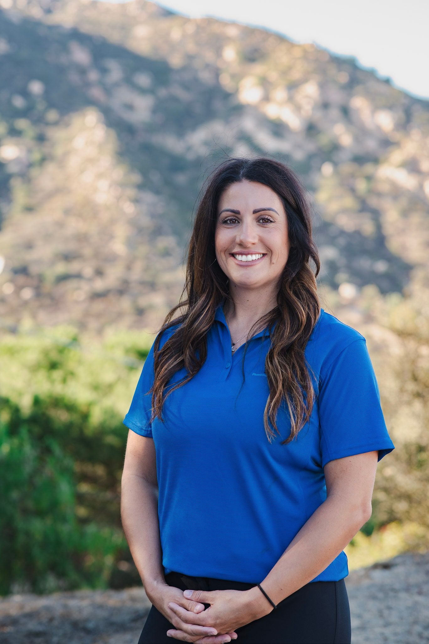 A woman in a blue shirt is standing in front of a mountain.