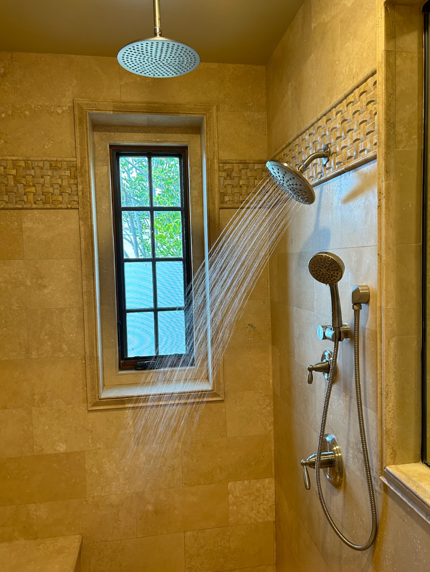 A shower head is spraying water in a bathroom next to a window.