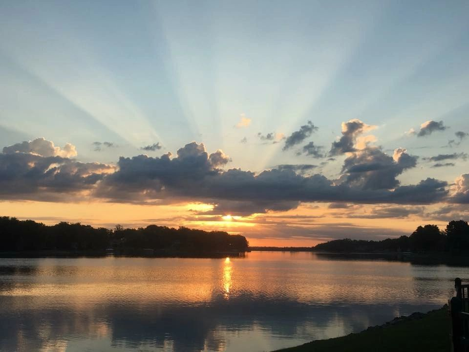 Sunset over a lake; orange and yellow sky with cloud rays reflecting on the water.