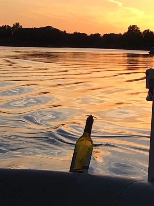 Wine bottle floating in rippled water at sunset.