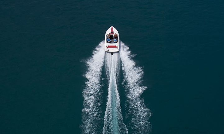 White motorboat speeding across teal water, leaving a white wake trail.