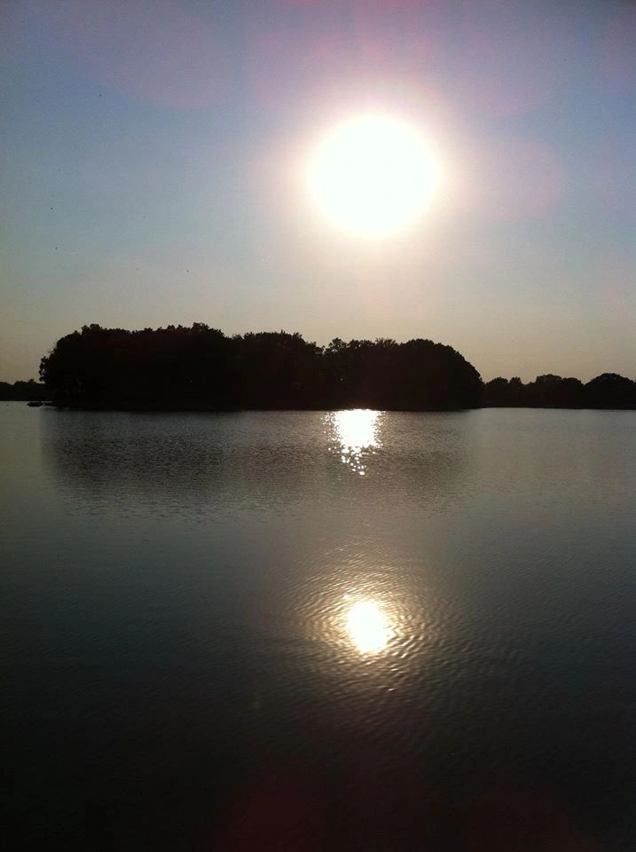Sun over a still lake with island and reflection. Evening sky.