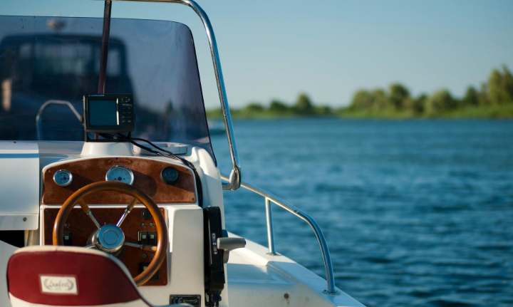 Steering wheel and dashboard of a boat on a blue lake, with trees in the background.