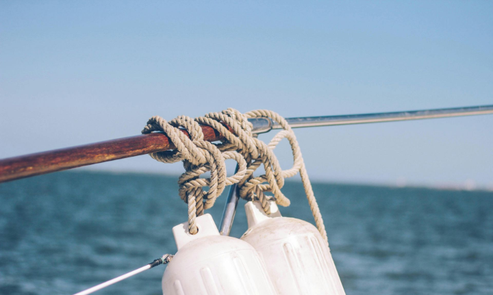 Two white boat fenders hanging from a rope tied to a wooden rail, blue water and sky in background.